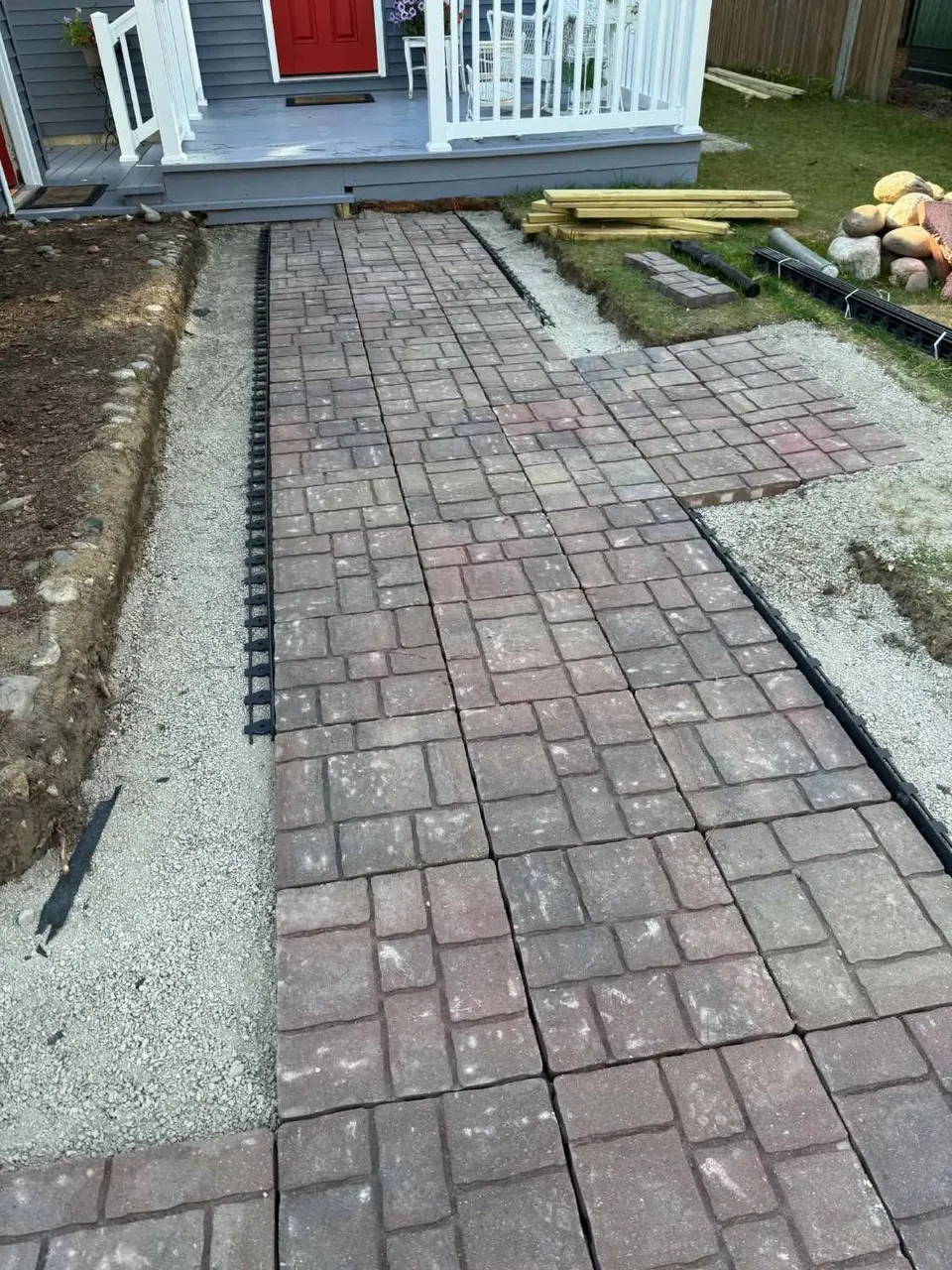 Paver walkway being installed over a compacted gravel base with black edge restraint