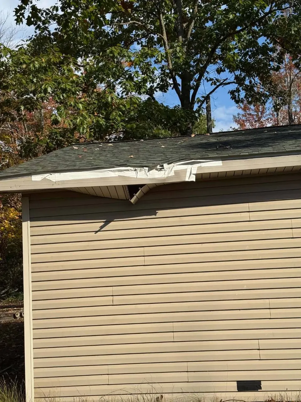 Tree limb damage to an outbuilding roof edge with a crushed gutter and open soffit