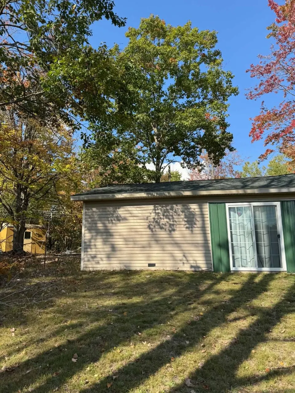 Outbuilding with its roof edge repaired under a large oak tree in fall