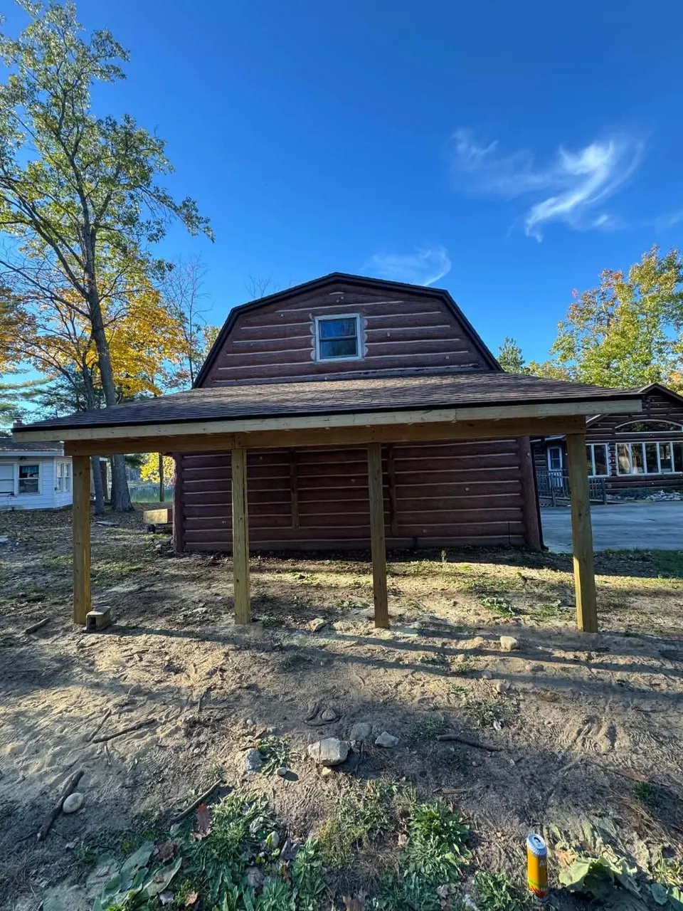 Lean-to framing with new posts, beam and rafters against a log-sided gambrel barn