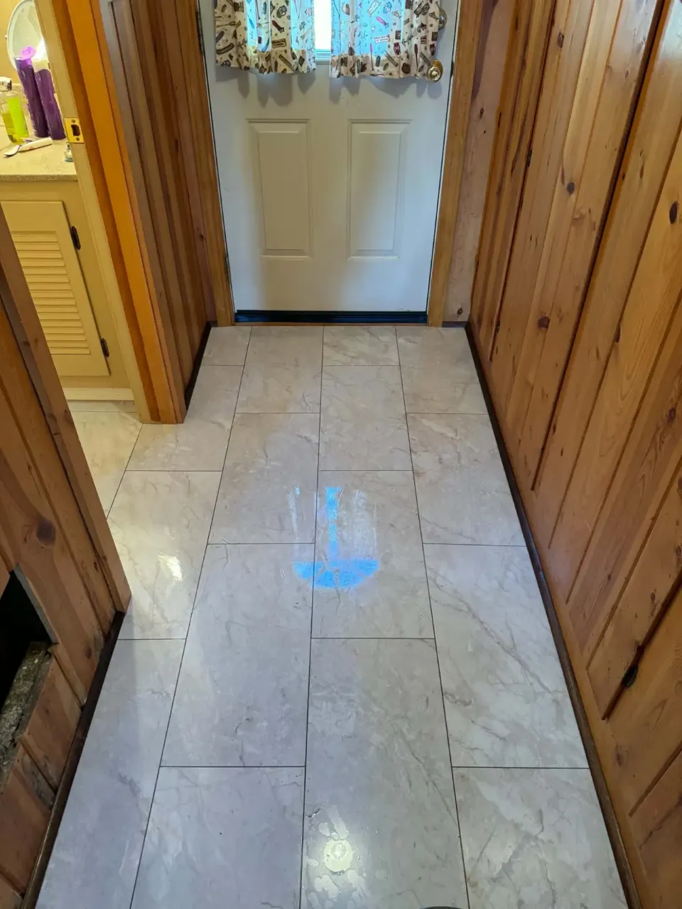 Hallway with glossy marble-look vinyl tile leading to a back door, knotty pine walls