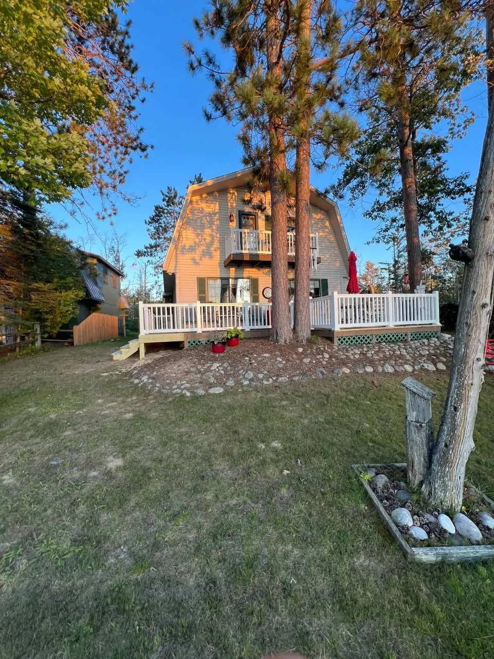 Gambrel-roof lake home with a deck, white vinyl railings and new stairs at sunset