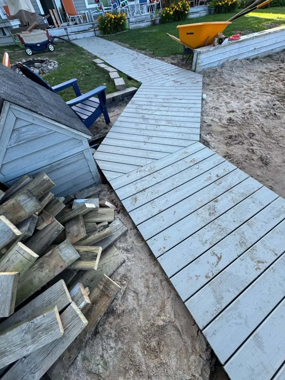 Gray composite boardwalk angling across sand from a lakeside lawn